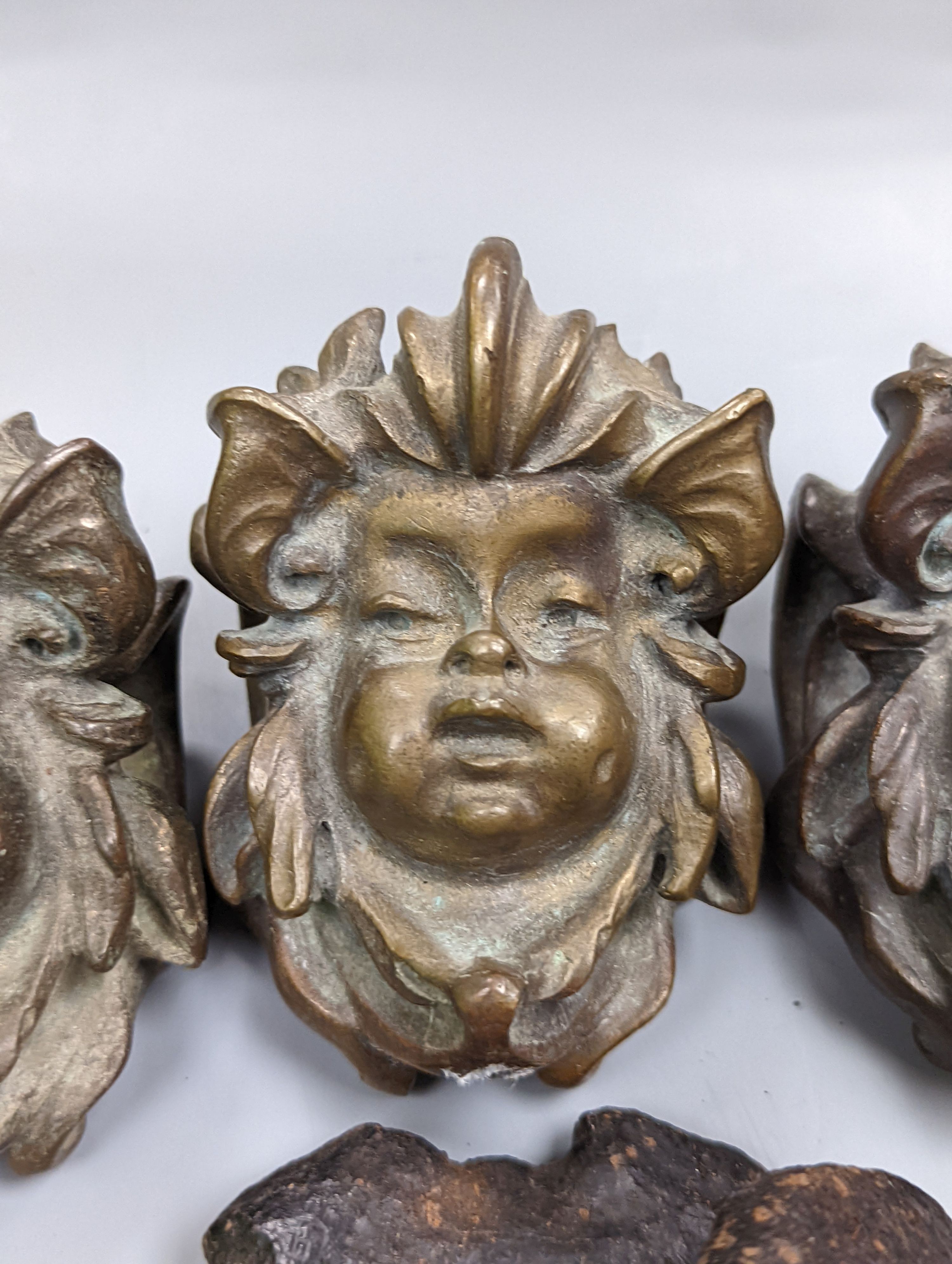 A set of three cast bronze mask-form furniture mounts, 9cm. high